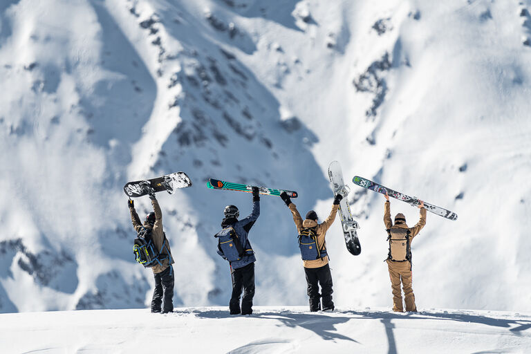 Skiers and snowboarders holding skis and boards in the air on a mountain ridge